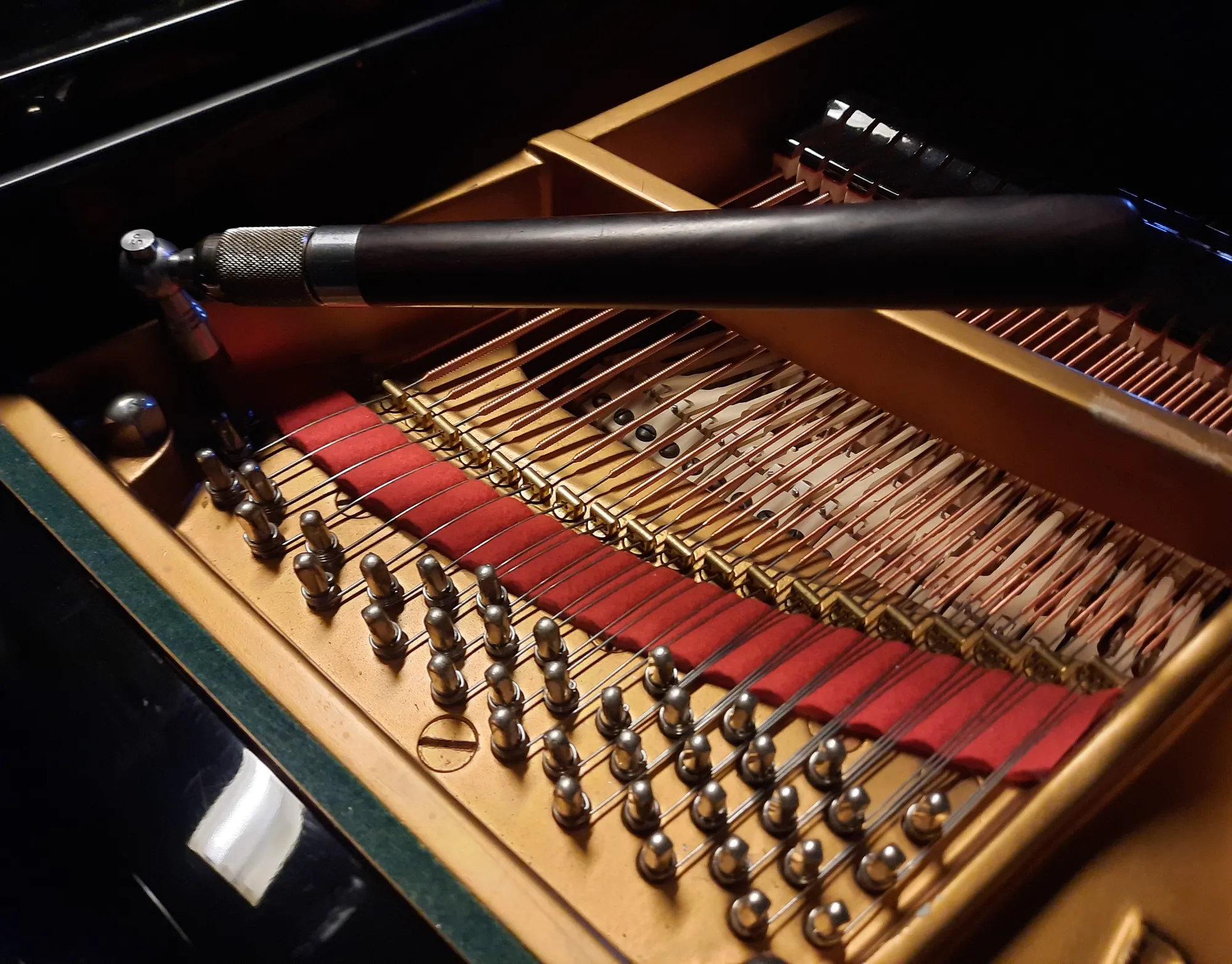 A tuning hammer resting on the tuning pins of a grand piano
